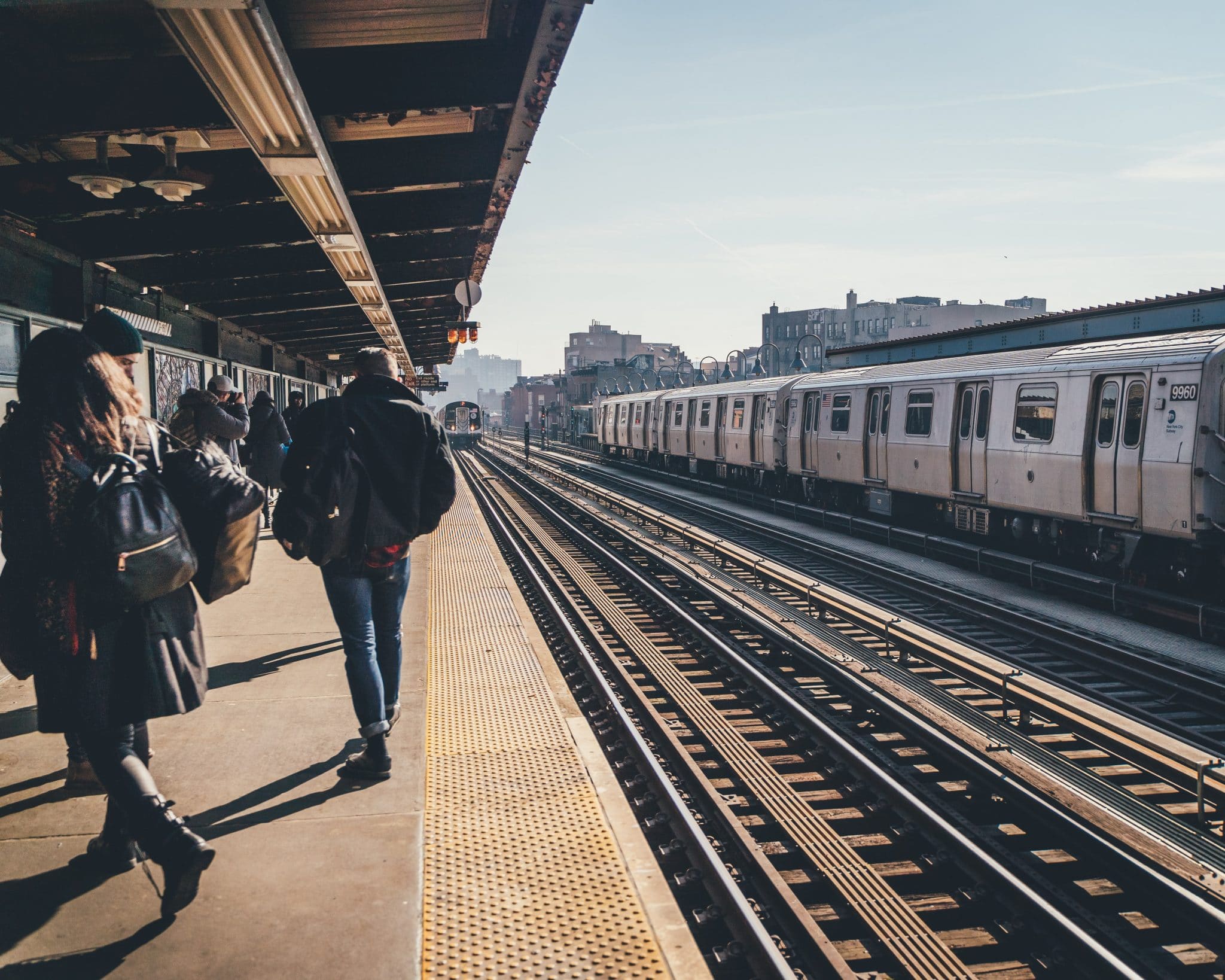 Outdoor New York City subway station platform with waiting and walking passengers