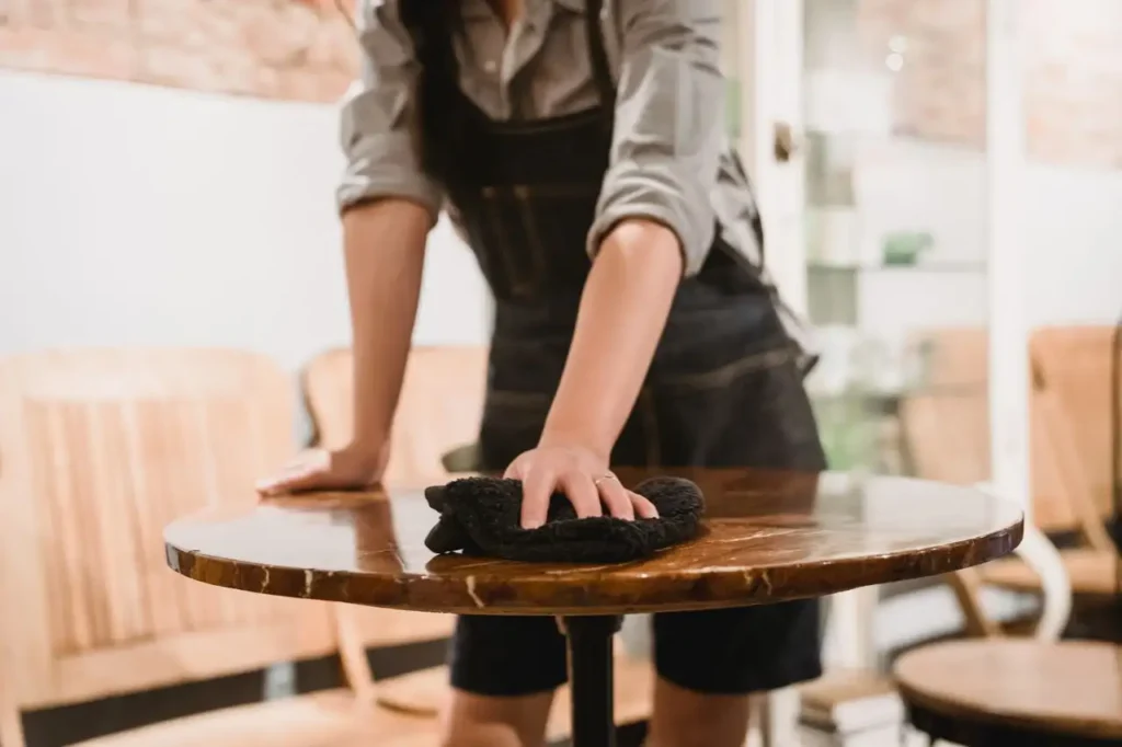 Person in apron cleaning a wooden table.