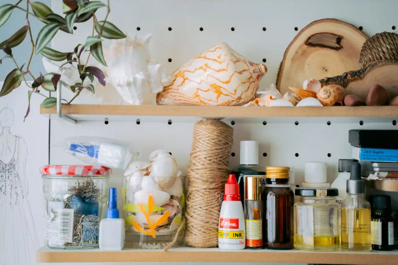 Pegboard storage wall with shelves holding household items, office supplies, and seashells