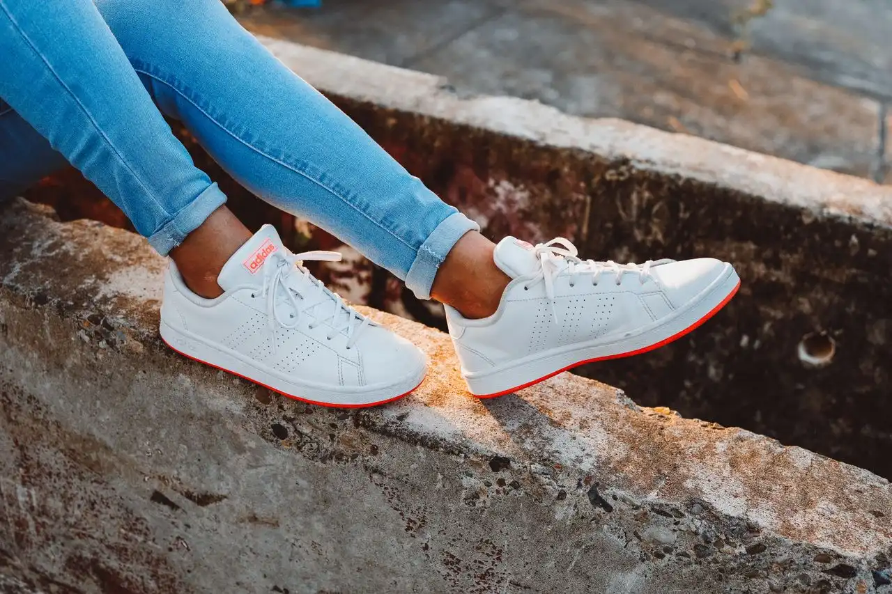 Person wearing sneakers sitting on a concrete barrier outdoors.